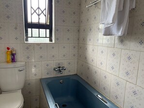 A bathroom with a toilet, a blue bathtub, and patterned tiles.