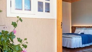 Ein Zimmer mit einem Bett, einem Fenster mit mattiertem Glas und einem Blumentopf mit rosa Blüten.