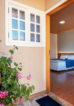 Ein Zimmer mit einem Bett, einem Fenster mit mattiertem Glas und einem Blumentopf mit rosa Blüten.