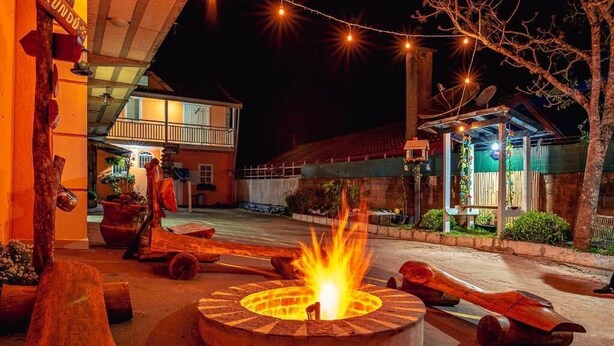 Una fogata en un patio con bancos de madera y un edificio al fondo.