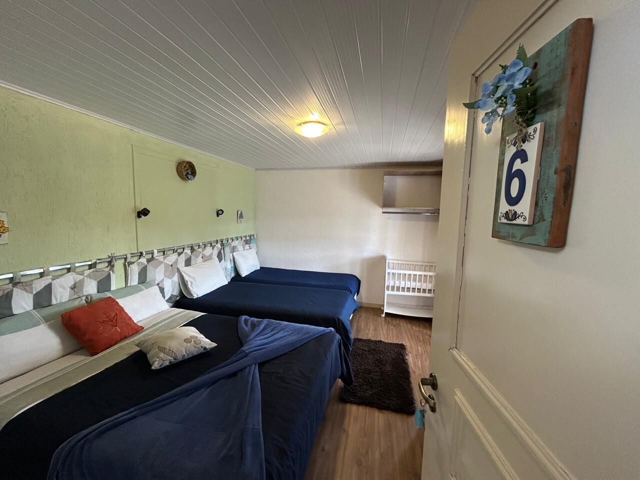 Habitación con dos camas, una cuna y un cartel numérico en la pared.