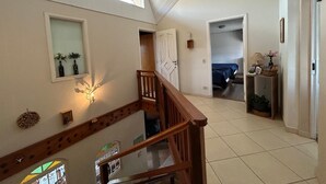 A spacious interior with a wooden staircase, a tiled floor, and a room with a bed and a lamp. - Skyblue Guesthouse by Concavus (Campos do Jordão)