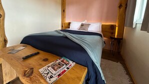 Un dormitorio con cama, mesita de noche de madera, control remoto y una revista.