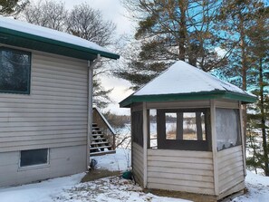 A cabin with a covered porch and a small shed, surrounded by trees and snow.