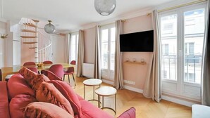 Una sala de estar moderna con un sofá rosa, un comedor con mesa y sillas, una escalera y ventanas grandes con cortinas.