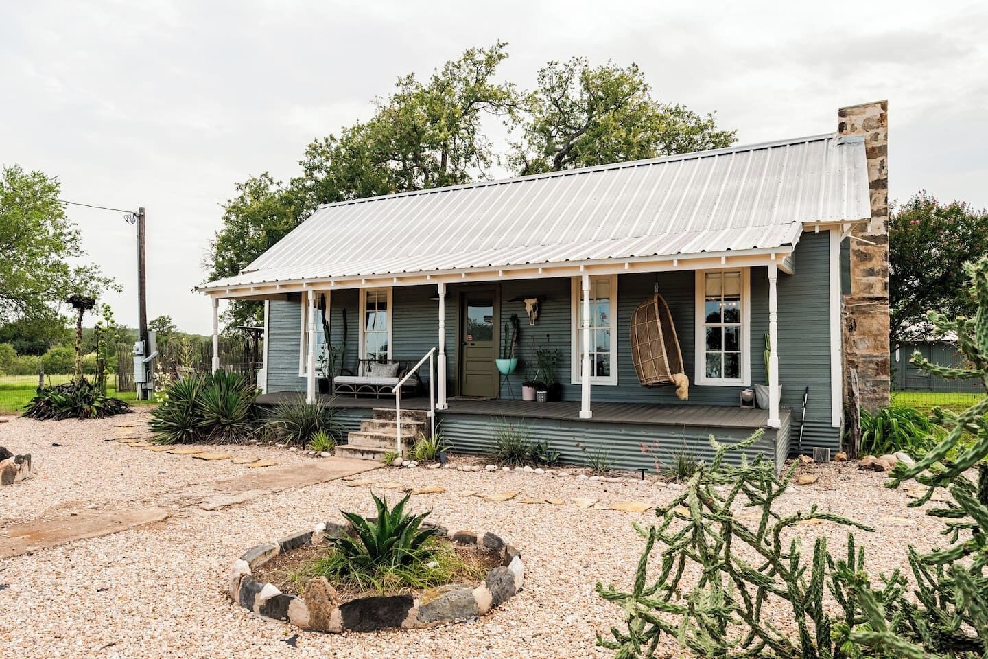 A rustic house with a porch, surrounded by desert plants and a gravel driveway.