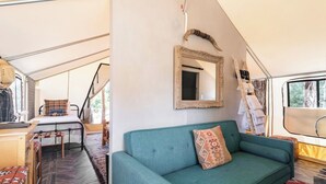 Un interior acogedor con un sofá, un espejo y una cama dentro de una estructura parecida a una tienda de campaña.