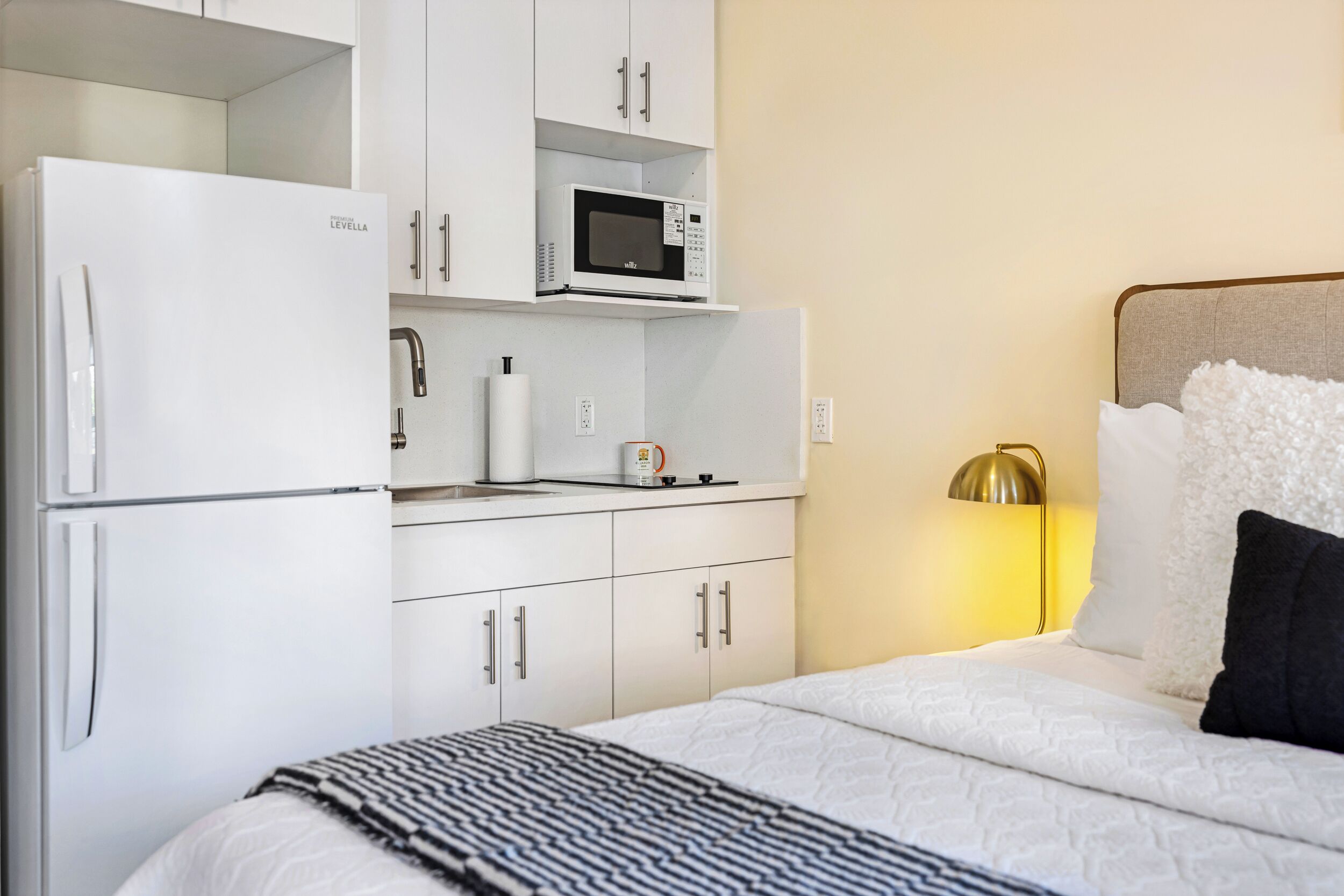 A bedroom with a bed, a white wardrobe, a microwave, and a bedside lamp.