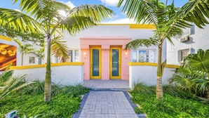 A building with a pink facade, yellow accents, and a paved entrance surrounded by greenery. - El Jardin Inn (Miami)