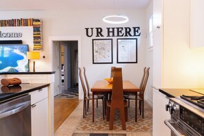 A modern kitchen with a dining table, chairs, and a 'UR HERE' sign above.