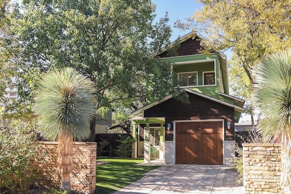 A two-story house with a green roof, a wooden garage door, and a stone wall.