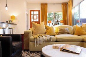 Ein Wohnzimmer mit einer Couch, Sesseln, einem Couchtisch und einem Fenster mit Vorhängen.