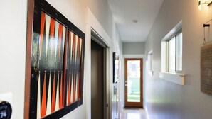 Um corredor com uma porta que dá para área externa, uma obra de arte emoldurada na parede e uma janela à direita.