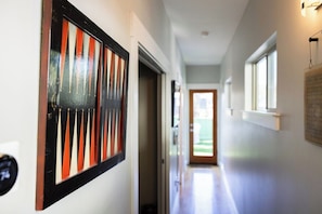Ein Flur mit einer Tür zu einem Außenbereich, einem gerahmten Kunstwerk an der Wand und einem Fenster auf der rechten Seite.