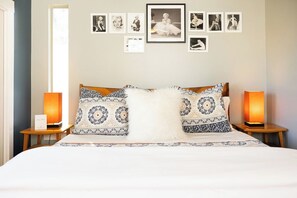 Ein Hotelzimmer mit einem Bett, gemusterten Kissen, Wandbildern und zwei Nachttischlampen.