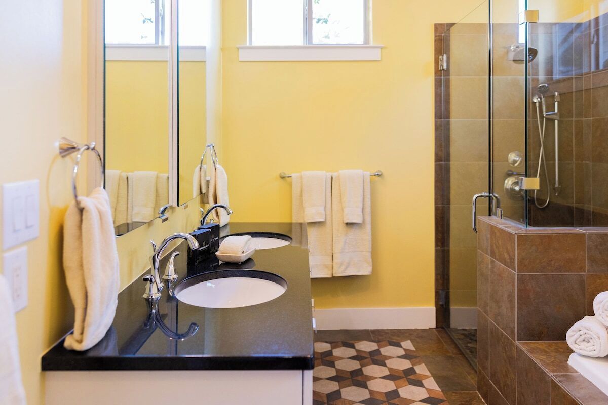 A bathroom with a black sink, two mirrors, a glass-enclosed shower, and a patterned floor.