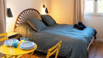 A bedroom with a bed, bedside lamps, a window, a table with chairs, and a dining table set with plates and glasses.