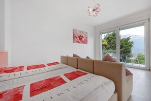 A bedroom with a bed, a ceiling light, a window with a view, and a door.