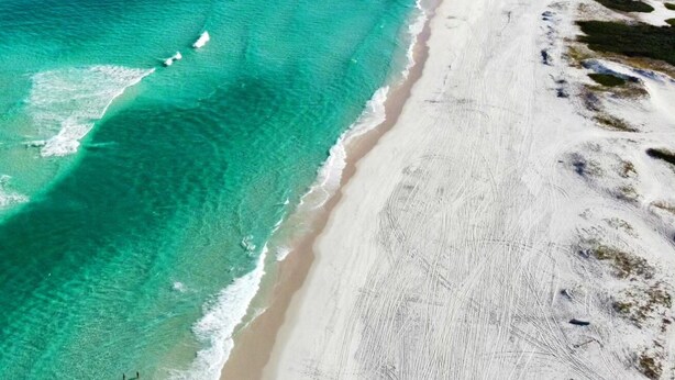Vista aérea de una playa con aguas turquesas cristalinas y una orilla arenosa.