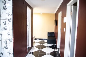 Un couloir avec un sol à carreaux, un canapé noir et une porte donnant sur une pièce dont le mur est jaune.