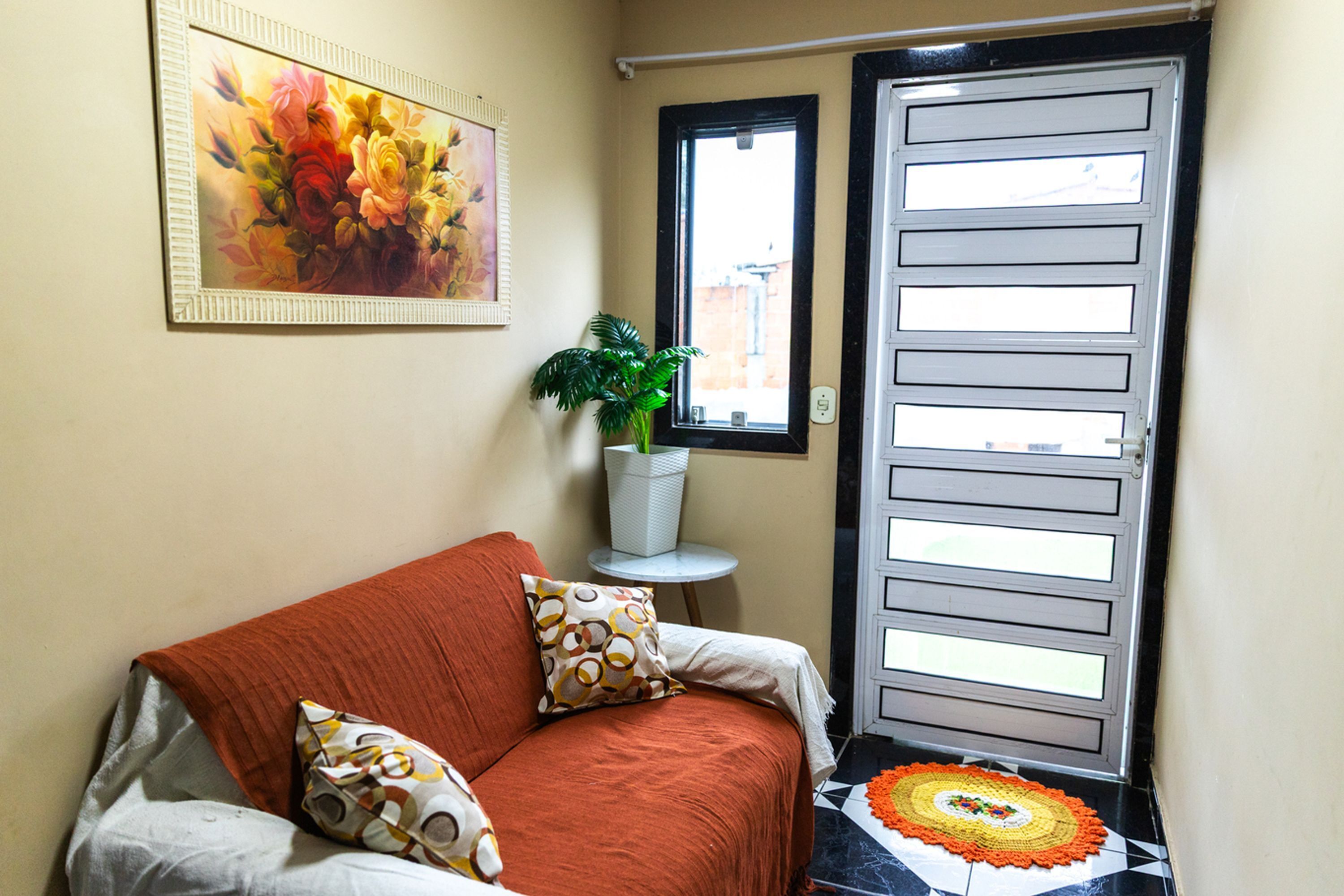 Ein Zimmer mit einer Couch, einem Blumentopf, einem gerahmten Gemälde und einer Tür mit Fenster.