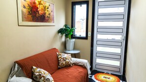 Una habitación con un sofá, una planta en maceta, un cuadro enmarco y una puerta con ventanal.