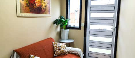 A room with a sofa, a potted plant, a framed painting, and a door with a window.