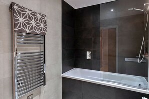 A modern bathroom with a glass-enclosed shower, a chrome towel rack, and dark tiled walls. - Plymouth Residence (Plymouth)