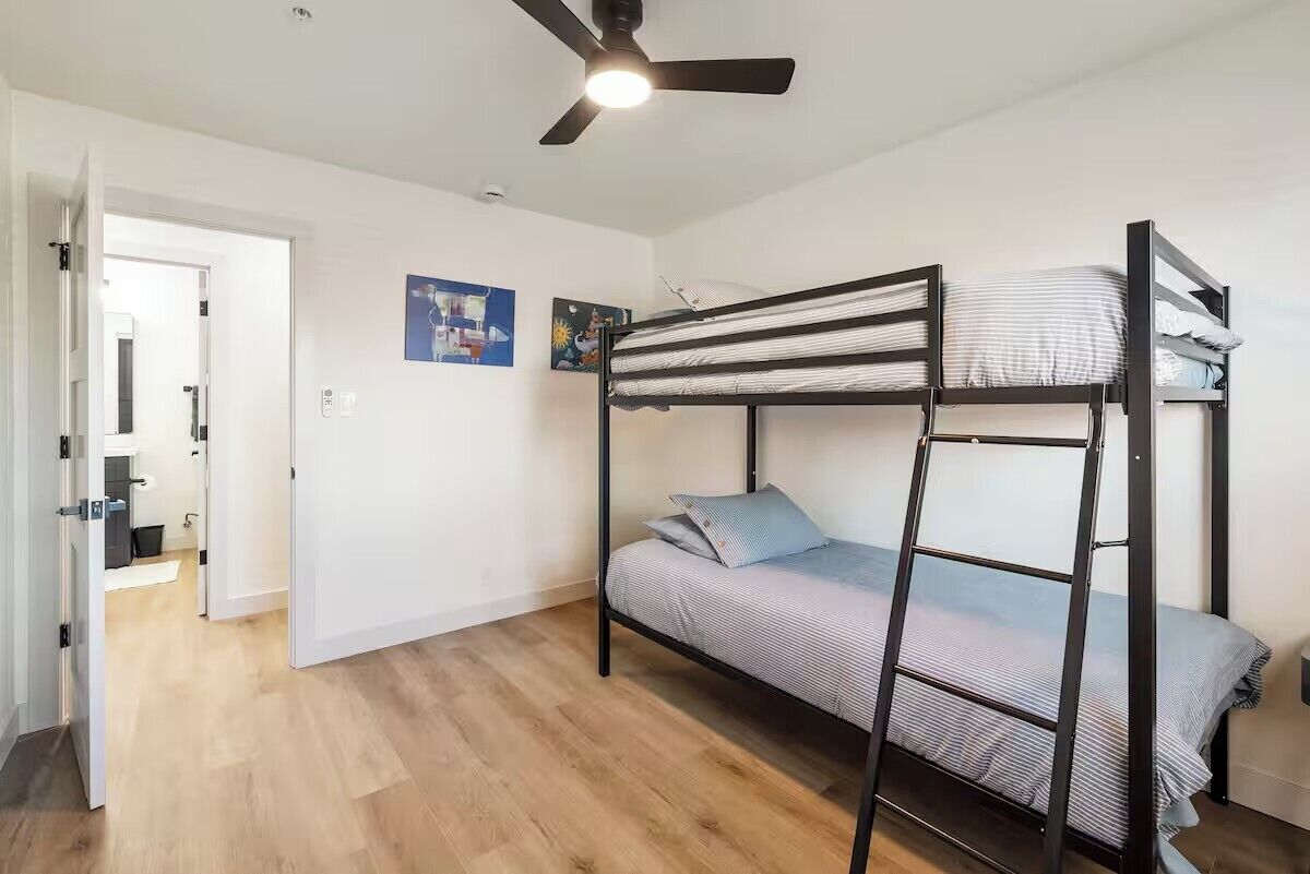 A bunk bed room with a ceiling fan, wooden flooring, and two wall art pieces.