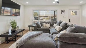 A modern living room with a grey sectional sofa, a black coffee table, and a ceiling fan. - Desert Dream- Retreat with Heated Pool (Scottsdale)