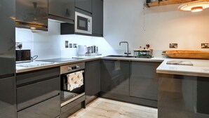 A modern kitchen with dark cabinets, a microwave, a sink, and a wooden cutting board. - Plymouth City Apartment 15 (Plymouth)