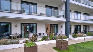 A modern two-story residential building with a patio area featuring outdoor furniture, planters, and a well-maintained lawn. - Plymouth City Apartment 15 (Plymouth)