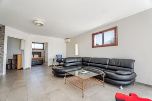 Un salon moderne avec un canapé d’angle en cuir noir, une table basse en verre et un fauteuil rouge.