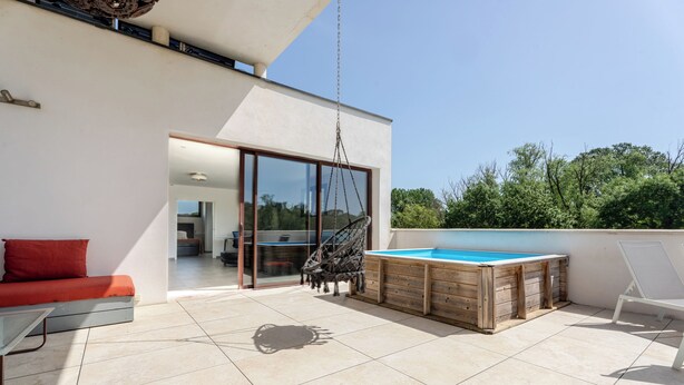 Een modern buitenterras met een jacuzzi, een hangstoel en een rode bank.