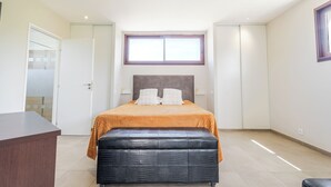 Een slaapkamer met een bed, een bankje, een bureau, een raam en een deur.