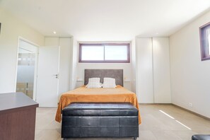Ein Schlafzimmer mit Bett, Sitzbank, Schreibtisch, Fenster und Tür.