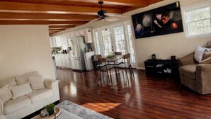 Een ruime woonkamer met een hoog houten plafond, een eettafel met stoelen, een bank en een salontafel.