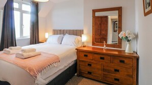 A hotel room with a bed, bedside table, dresser, mirror, and a window with curtains. - Scamnel (Stone)