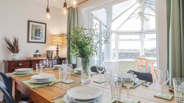 A dining area with a wooden table set for a meal, a large window with a view, and a ceiling fan. - Scamnel (Stone)
