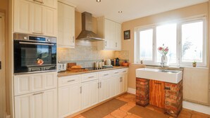 A kitchen with white cabinets, a brick island, a window with a view, and a tiled floor. - Scamnel (Stone)