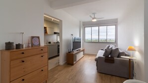 Een moderne woonkamer met een grijze bank, een houten dressoir en een televisie op een meubel. Een raam biedt uitzicht op de omgeving.