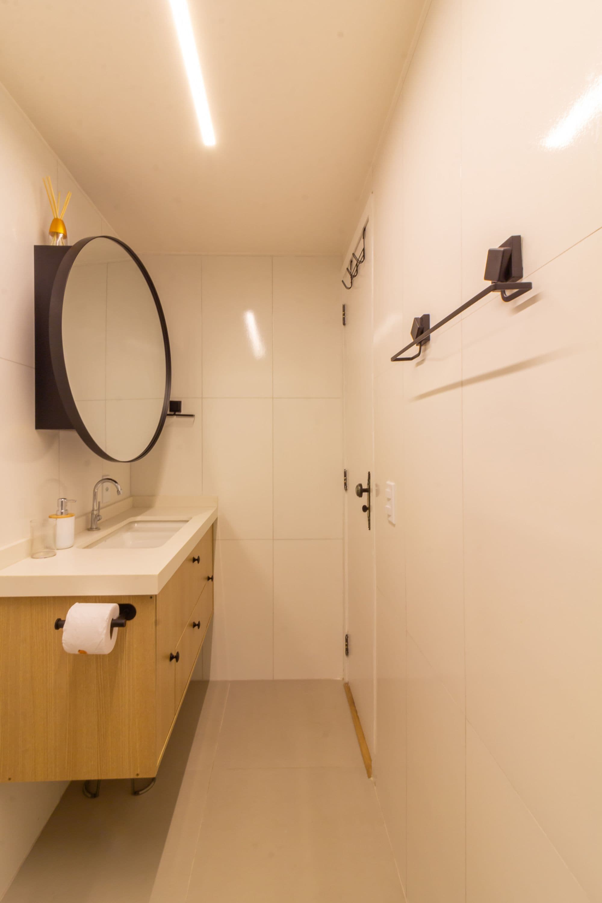Ein modernes Badezimmer mit einem Holzbadschränkchen, einem runden Spiegel, einer Toilette und einer Duschkabine.