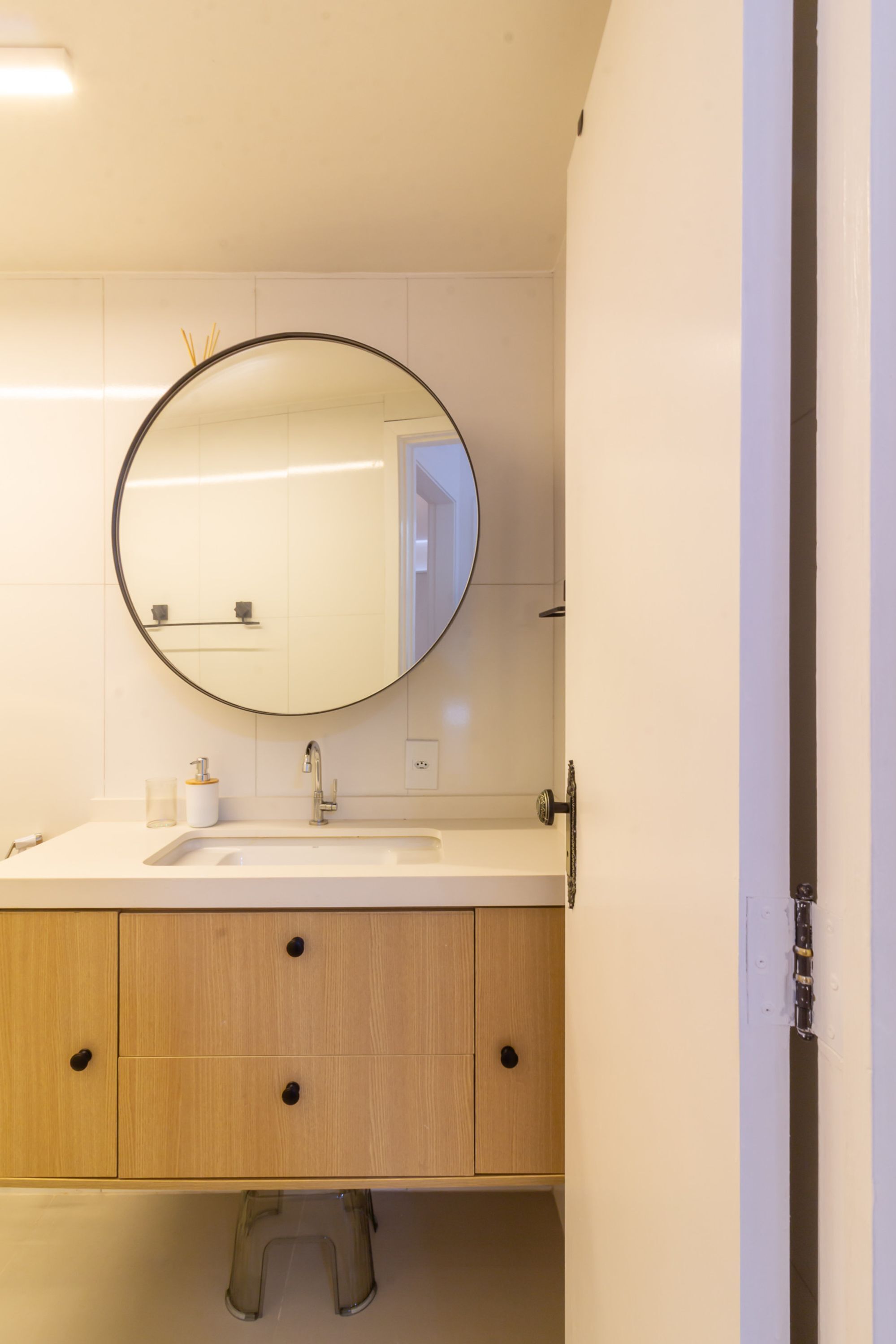 A bathroom with a round mirror, a white sink, and wooden cabinets.