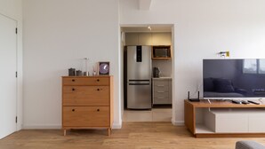 Een moderne woonkamer met een houten kast, een flatscreen televisie en een keuken met een koelkast en magnetron.