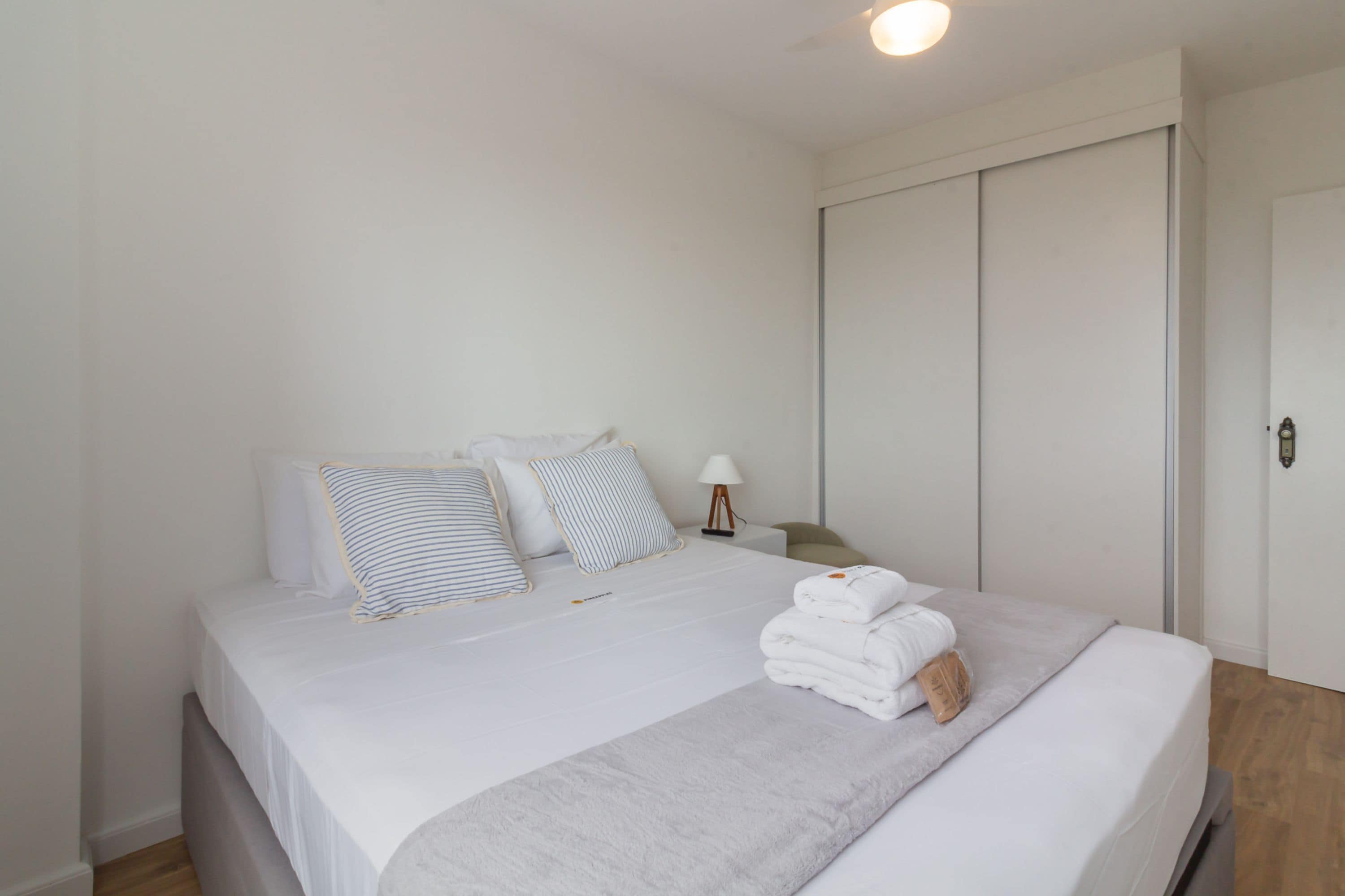 A neatly made bed with white linens, striped pillows, and a folded towel on the side.