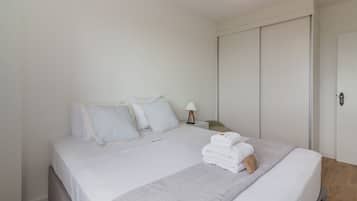 A neatly made bed with white linens, striped pillows, and a folded towel on the side.
