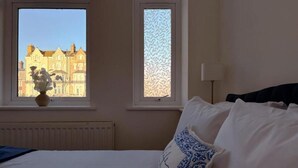 Une chambre d’hôtel avec un lit, une fenêtre donnant sur des immeubles, un radiateur et une lampe.