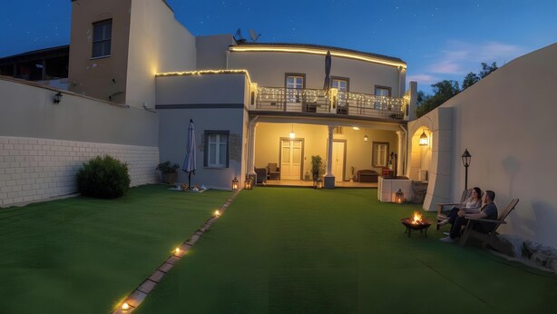 Une maison à deux étages avec un balcon, une pelouse bien entretenue et un espace extérieur aménagé pour s’asseoir.