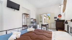 Une chambre d’hôtel comprenant un lit, un téléviseur à écran plat, un bureau avec une chaise, une petite table et une armoire.