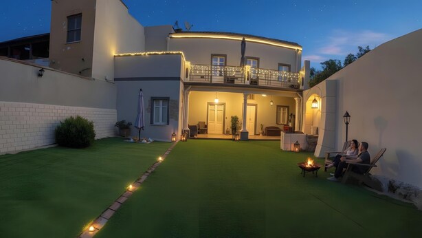 A two-story house with a balcony, a well-maintained lawn, and outdoor seating area. - Room 5 – Double Room with Garden View (Assemini)